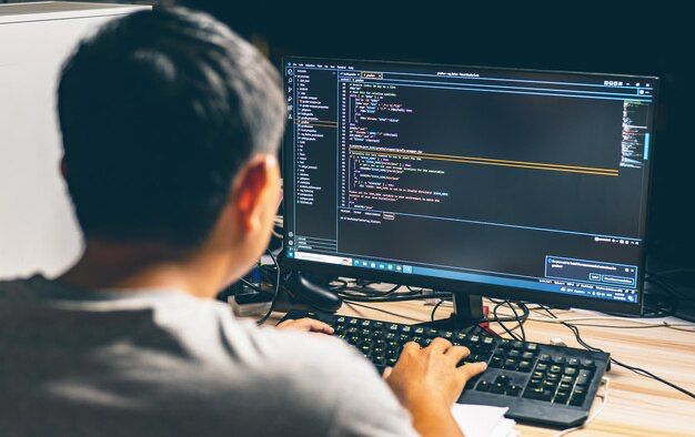 Rear view of a man writing program code on a computer