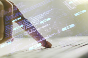 A finger presses the keyboard, program code is in the foreground